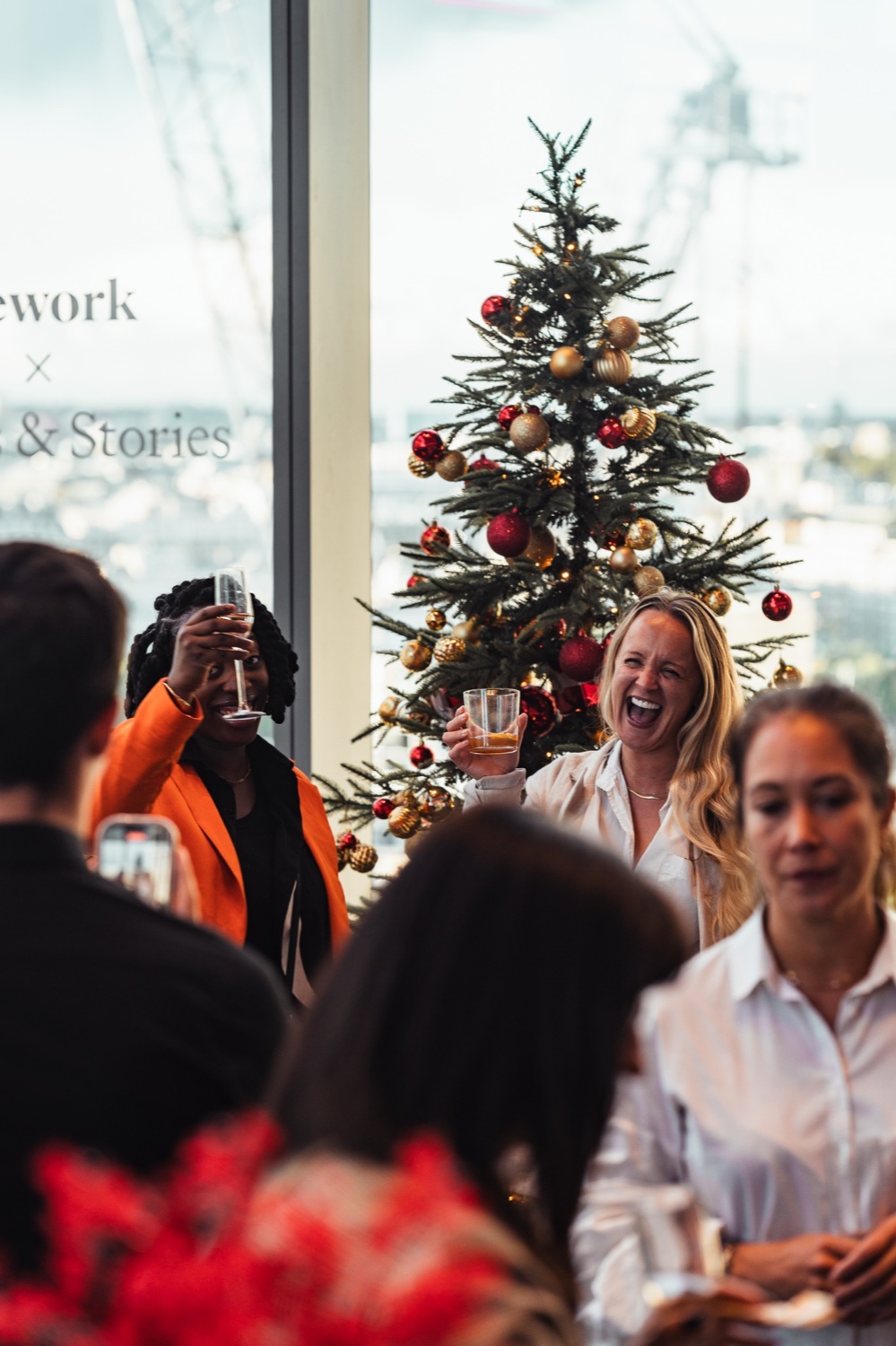 Guests laughing and raising their drinks beside a decorated Christmas tree