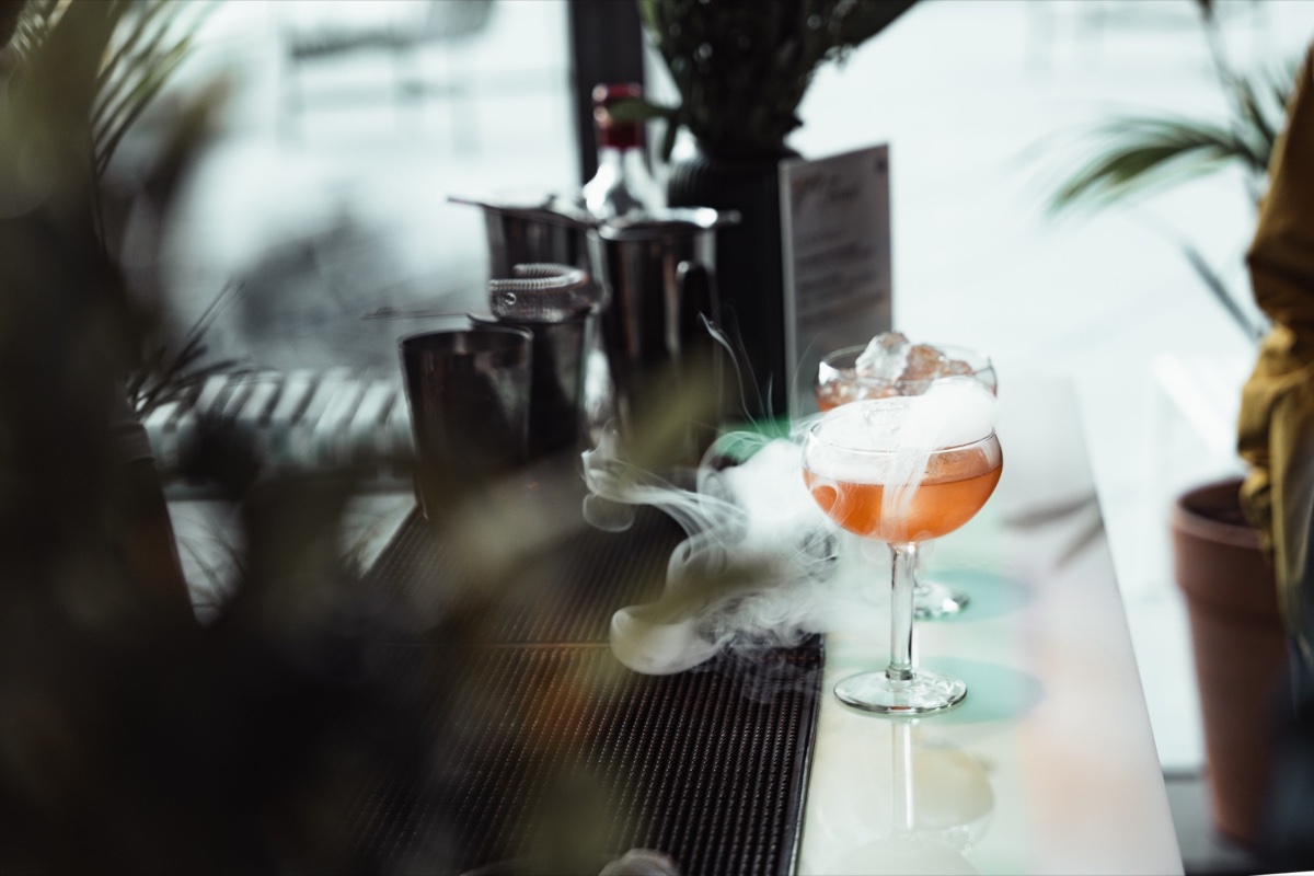 A freshly prepared orange cocktail with smoke curling around its stemmed glass